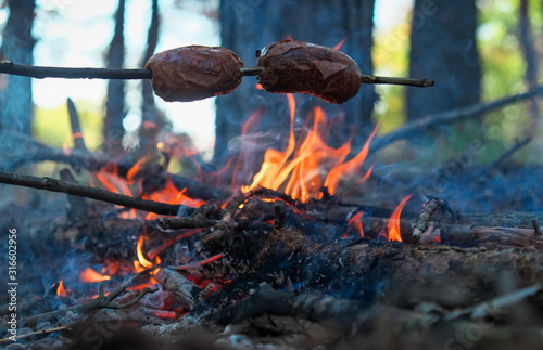 Fry sausages in nature. Barbecue and kebabs in travel. Leisure. Camping in the forest, touristic view, concept of travel and freedom