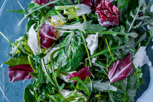 Salad of fresh arugula, spinach, iceberg lettuce, radicio salad with ginger and lemon dressing on a transparent plate on a blue background. Soft focus. The concept of veganism and raw food diet. photo