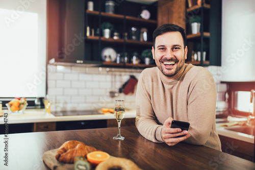 Happy man using phone and drinking wine in the kitchen