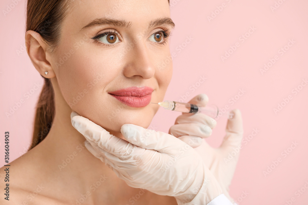 Young woman receiving filler injection against color background Young woman receiving filler injection against color background