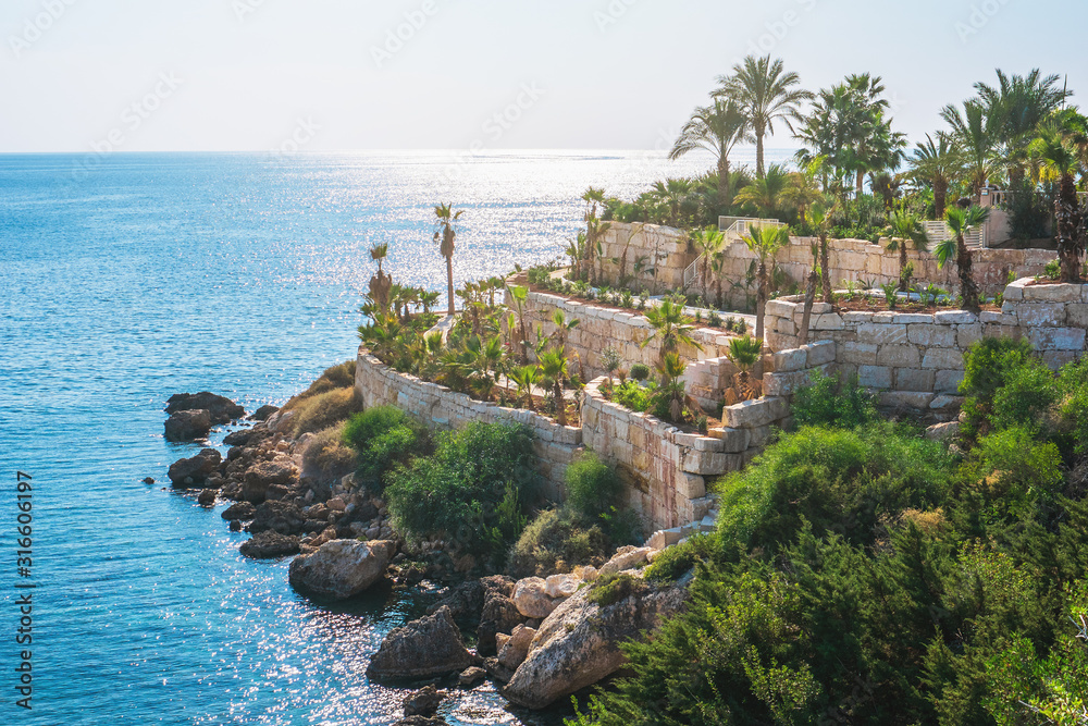 Cyprus landscape. Beautiful structure on hill of masonry with multi-level paths and palm trees near Mediterranean sea coast in sunny day.