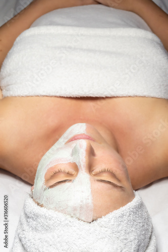 Woman lies with cosmetic mask applied on half face in beauty salon