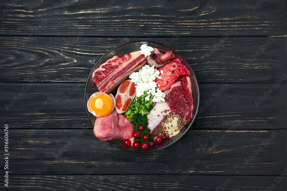 Dog food. Natural Organic Raw meat and dairy products, fish, egg, vegetables and supplements. Black wooden background. Close up. - obrazy, fototapety, plakaty 