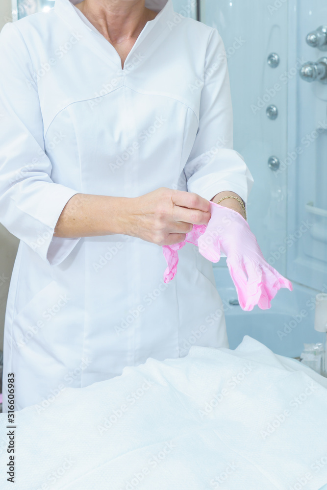 Cosmetologyst puts on medical latex pink gloves. Preparation for procedures in the cosmetologist's office