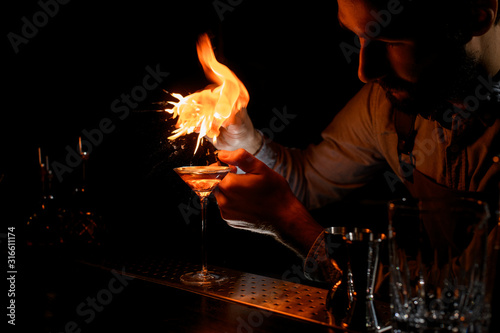 Male bartender spraying on a lighter with orage zest juice to the golden alcoholic drink in a martini glass