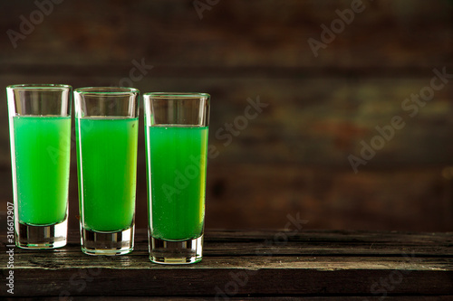Green cocktail with kiwi in three glasses on a wooden board. Green cocktail with kiwi on a wooden board background. Green smoothie with kiwi and martini.