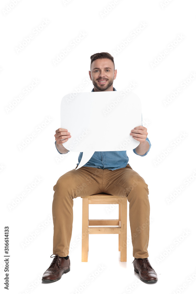 smiling casual man sitting an presenting a blank speech bubble on white background smiling casual man sitting an presenting a blank speech bubble on white background