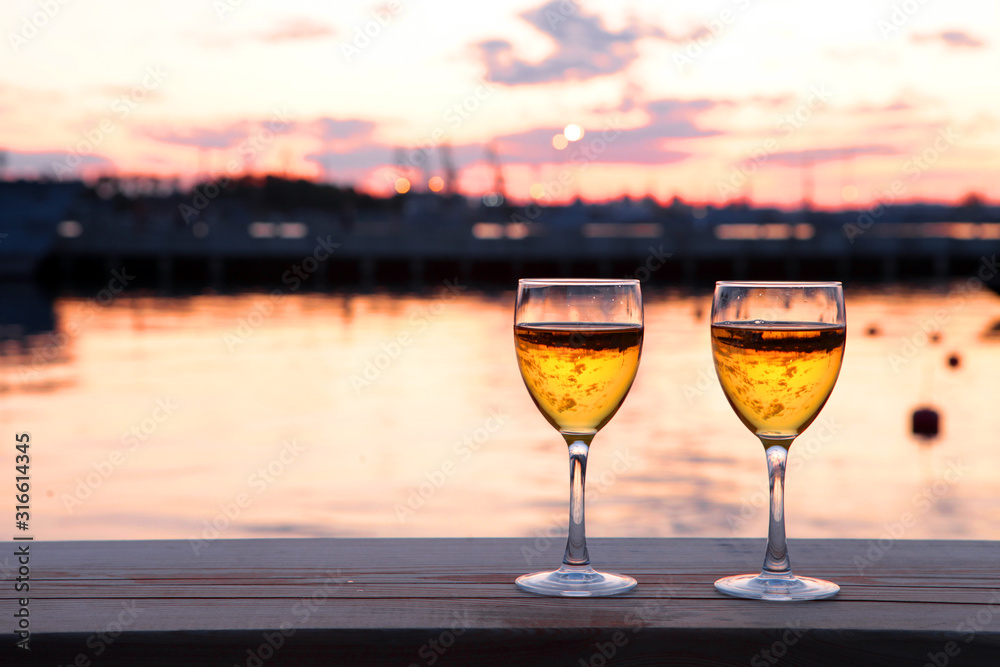 Two Glasses of white wine and drops of ice cubes against red sunset in yachting port. Beautiful summer evening sea view. Vacation for couple. Romantic evening