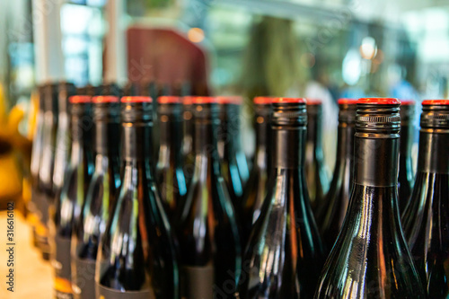 dark black amber glass wine bottles top, with red screw cap seal, close up and selective focus view, new bottle winery tasting room display background