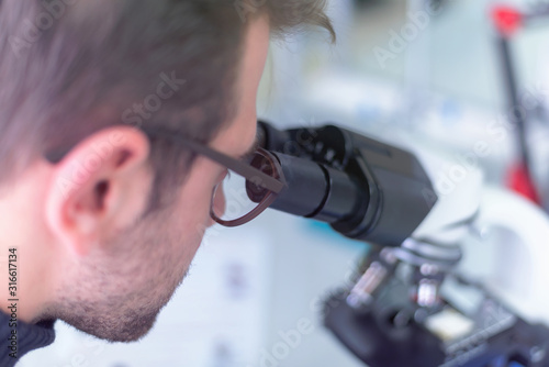 Fototapeta Naklejka Na Ścianę i Meble -  Young male scientist looking through a microscope in a laboratory doing research, microbiological analysis, medicine.