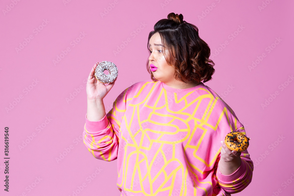 Sad plus size model with doughnuts, fat woman sadness and overeats on pink background Sad plus size model with doughnuts, fat woman sadness and overeats on pink background