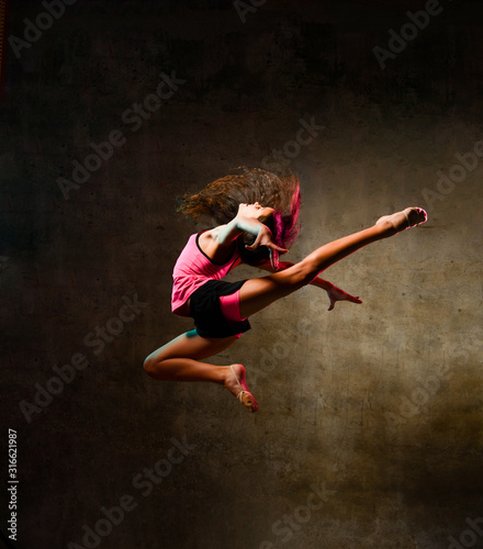 Fototapeta Naklejka Na Ścianę i Meble -  Street dance girl dancer jumping up dancing in neon light doing gymnastic exercises jump in studio on dark wall