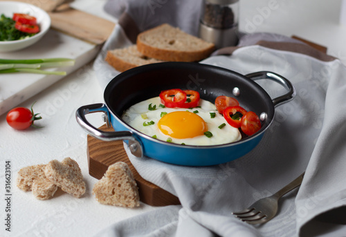 Fried egg with tomato, green onion, red pepper in frying pan, slices of bread in shape of heart. Tasty breakfast photo