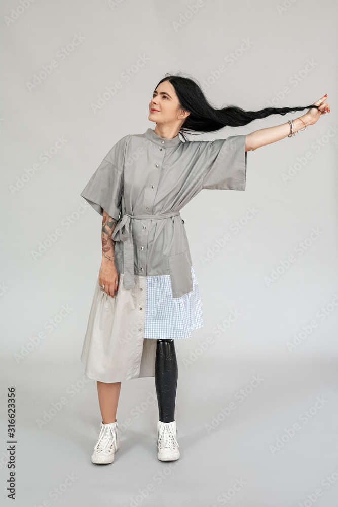 Freestyle. Diverse girl with leg prosthesis standing isolated on grey full body shot holding hair aside smiling playful Freestyle. Diverse girl with leg prosthesis standing isolated on grey full body shot holding hair aside smiling playful