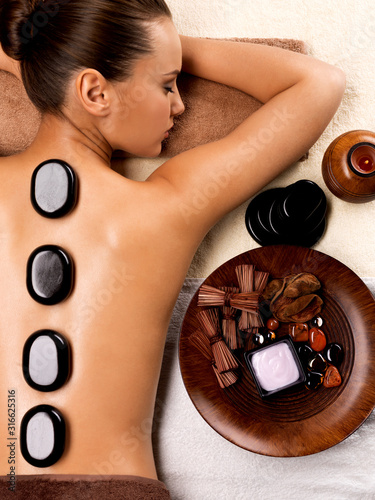 Beautiful woman relaxing in spa salon with hot stones on body.