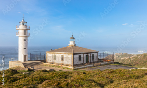The Tourinan lighthouse in Galicia in northern Spain. It is a sunny winter afternoon. The air is very hazy with a lot of spray from the Atlantic. There are high waves on the sea.