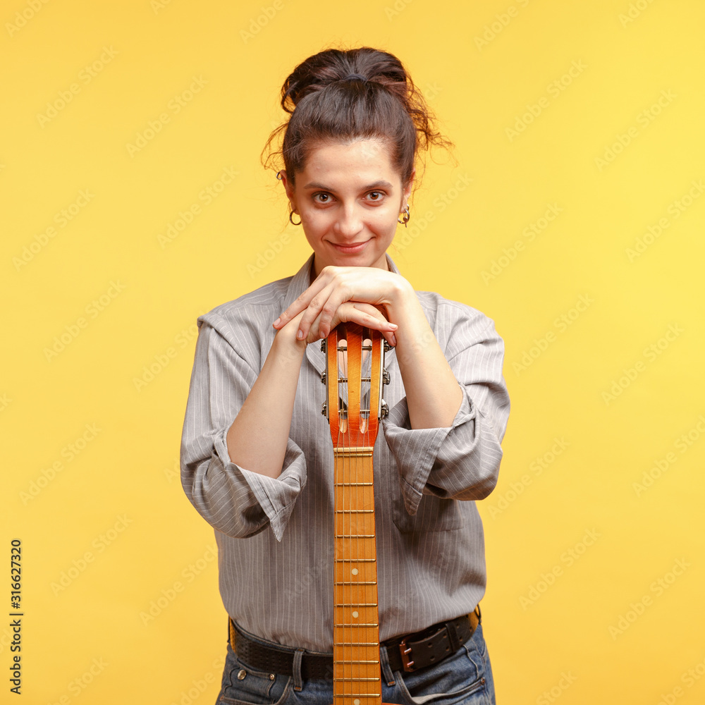 young attractive girl with dark curly hair with an acoustic guitar. Studio shooting yellow background. young attractive girl with dark curly hair with an acoustic guitar. Studio shooting yellow background.