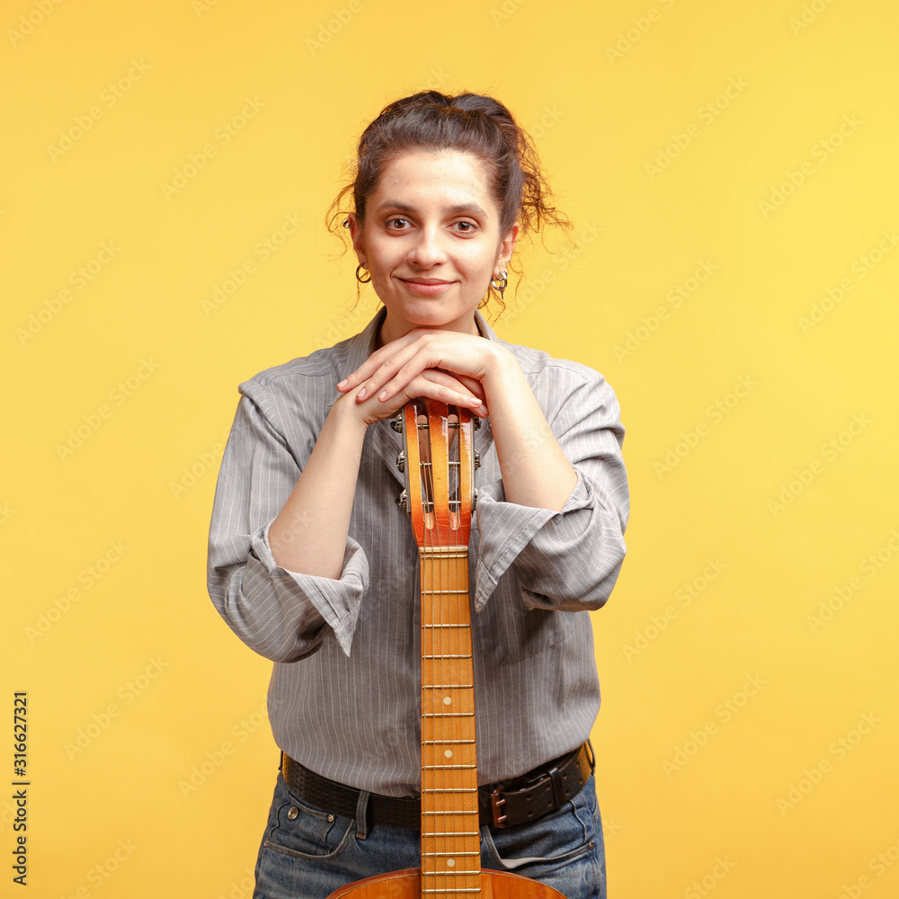 young attractive girl with dark curly hair with an acoustic guitar. Studio shooting yellow background. young attractive girl with dark curly hair with an acoustic guitar. Studio shooting yellow background.