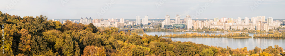 Naklejka premium View from the high hills, covered with dense forest, on the buildings and structures of a large city on the river