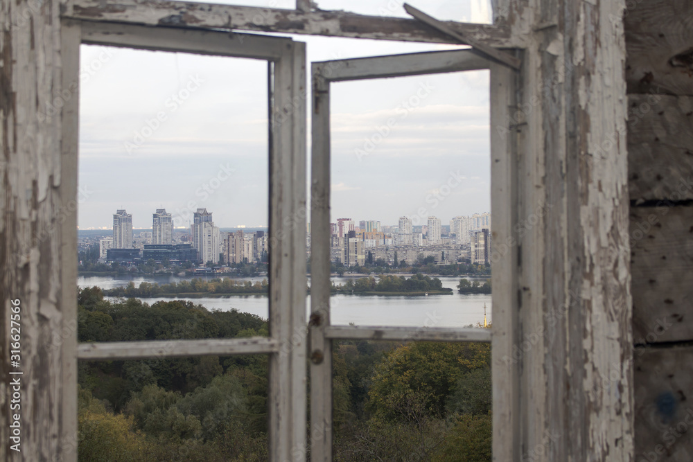 View from an old broken window on the park's topography, a river with islands and multi-storey modern buildings