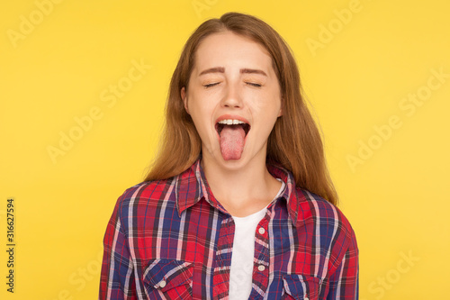 Fotografie Portrait of naughty disobedient ginger girl in casual shirt standing with closed eyes and sticking out tongue, looking funny childish with derisive grimace