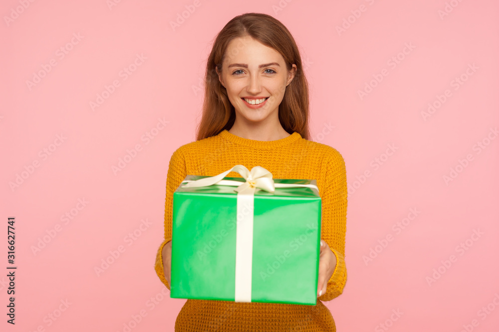 Portrait of cheerful pretty ginger girl holding big gift box and looking at camera with toothy smile, showing green present, greeting and celebrating holiday. studio shot isolated on pink background Portrait of cheerful pretty ginger girl holding big gift box and looking at camera with toothy smile, showing green present, greeting and celebrating holiday. studio shot isolated on pink background