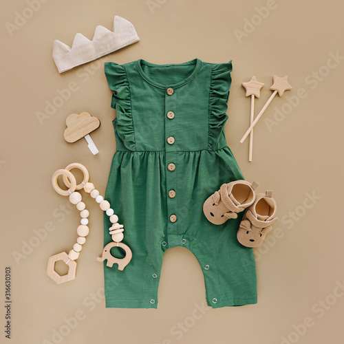 Green romper  with   wooden toys and baby shoes. Set of baby clothes and accessories on beige background.  Fashion newborn. Flat lay, top view photo