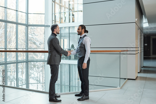 Two young elegant business partners shaking hands while greeting one another