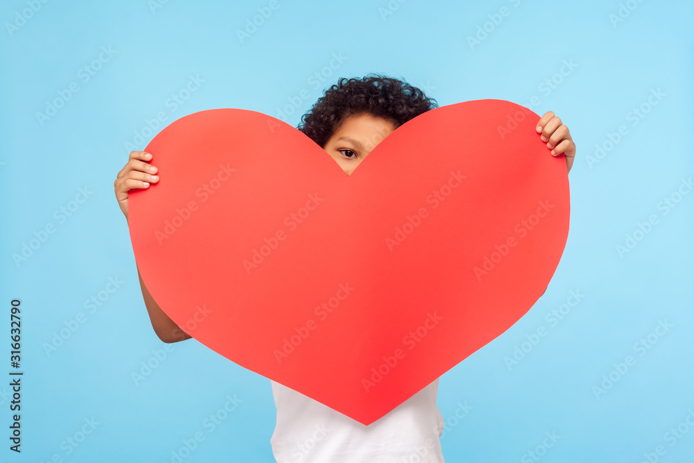 © khosrork - Cute shy adorable little boy peeking out from big red paper heart, unrecognizable child holding symbol of love, charity, looking with interest at camera. indoor studio shot isolated on blue background © khosrork - Cute shy adorable little boy peeking out from big red paper heart, unrecognizable child holding symbol of love, charity, looking with interest at camera. indoor studio shot isolated on blue background