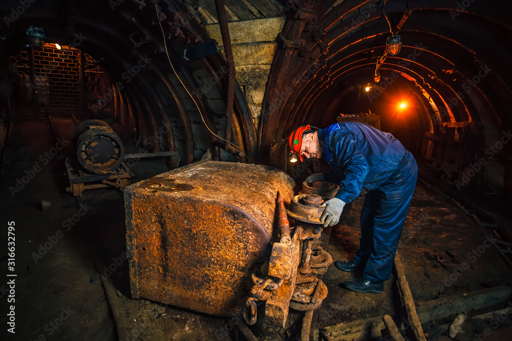 A miner in a coal mine stands near a trolley. Copy space. Miner repairing a trolley A miner in a coal mine stands near a trolley. Copy space. Miner repairing a trolley