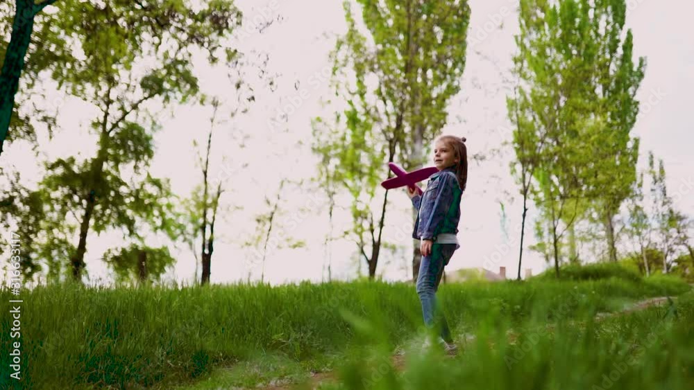 Little girl launches a toy plane into the air in the park outdoor. Child launches a toy plane. Beautiful little girl running on the grass and launches a pink toy plane. Slow motion