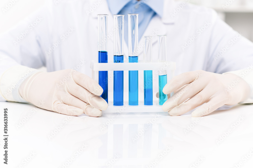 Gloved hands of contemporary clinician sitting by desk and working with fluids