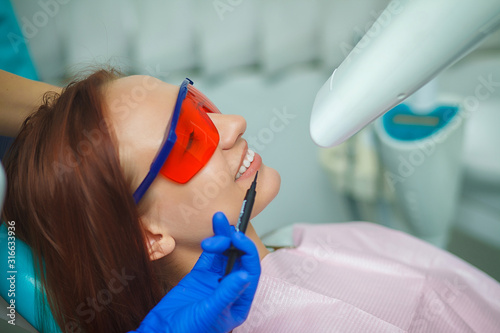 Beautiful girl in a red protective glasses sitting in a blue chair in the office of the dentist.