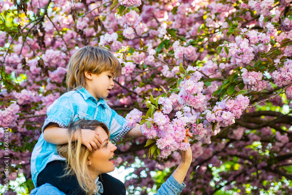 Mothers day. Mother and son. Happy mother giving shoulder ride on his shoulders in sakura garden. Mothers day. Mother and son. Happy mother giving shoulder ride on his shoulders in sakura garden.
