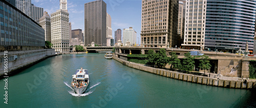 This is a tour boat on the Chicago River during summer. The Chicago Tribune Building, Chicago Sun Times Building, and the IBM Building surround the river. photo