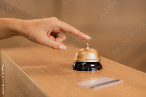 Hand of young contemporary businesswoman over call ring on reception counter