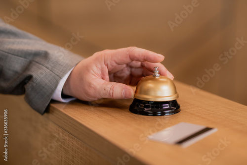 Hand of traveling businessman pushing ring button on wooden reception counter
