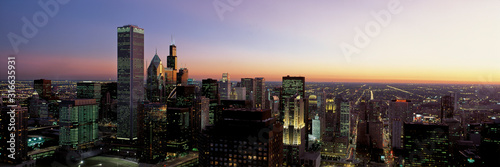 This is an aerial view of the skyline with the Sears Tower at sunset. It is a summer evening and the lights of the city are on.