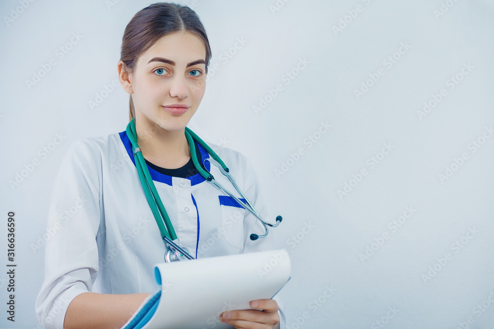 Doctor with a stethoscope, holding a notebook in his hand. Close-up of a female doctor filling up medical form at clipboard while standing straight in hospital