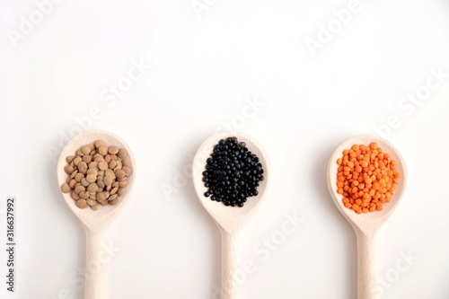 Three wooden spoons with lentils of different varieties, orange, black and brown on a white background. Place for text