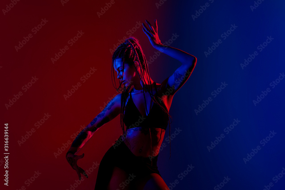 Black dressed and braided hair woman dancing on a blue and red background.