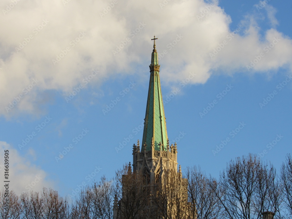 The green spire of the American Church in Paris with blue sky and clouds in the background 