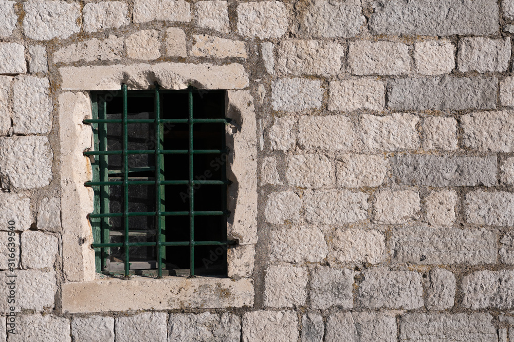 Old window with bars, in an ancient medieval wall