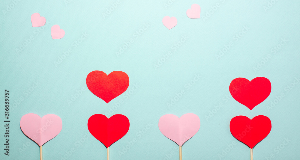 Paper hearts of different sizes fly up from red and pink hearts on wooden sticks on blue background. Valentines day concept. Flat lay