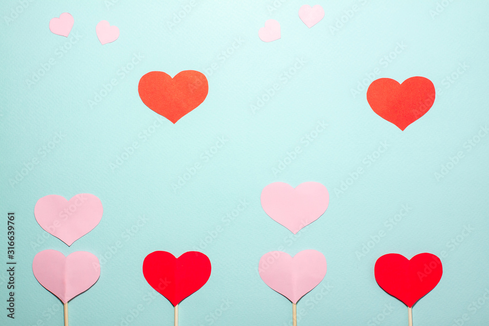 Paper hearts of different sizes fly up from red and pink hearts on wooden sticks on blue background. Valentines day concept. Flat lay top view