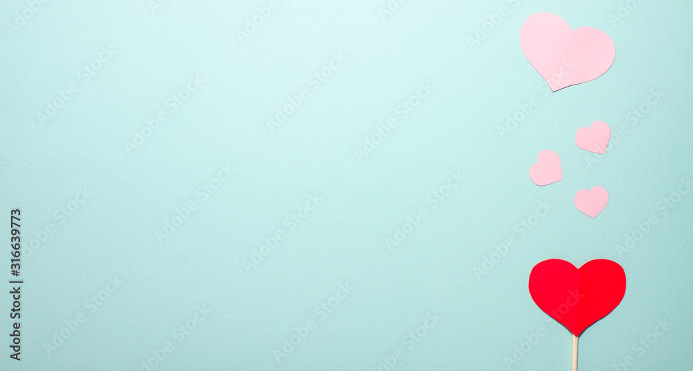 Hearts of different sizes fly up from a red paper heart on wooden stick on the right side on blue background. Valentines day concept. Flat lay top view with space for text banner
