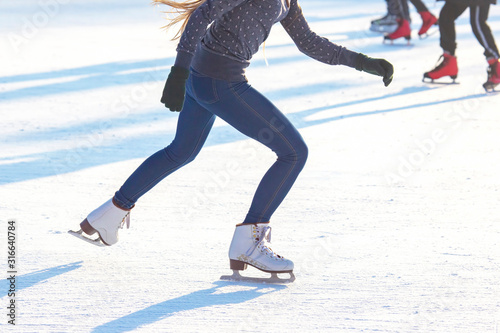 girl in blue jeans actively skates on white skates on an ice rink. Sport and hobbies. Holidays and winter fun