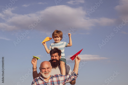 Happy smiling boy on shoulder dad looking at camera. Male multi generation portrait. Boy with father and grandfather.