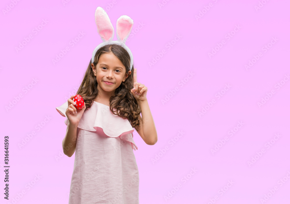 Brunette hispanic girl wearing easter rabbit ears surprised with an idea or question pointing finger with happy face, number one Brunette hispanic girl wearing easter rabbit ears surprised with an idea or question pointing finger with happy face, number one