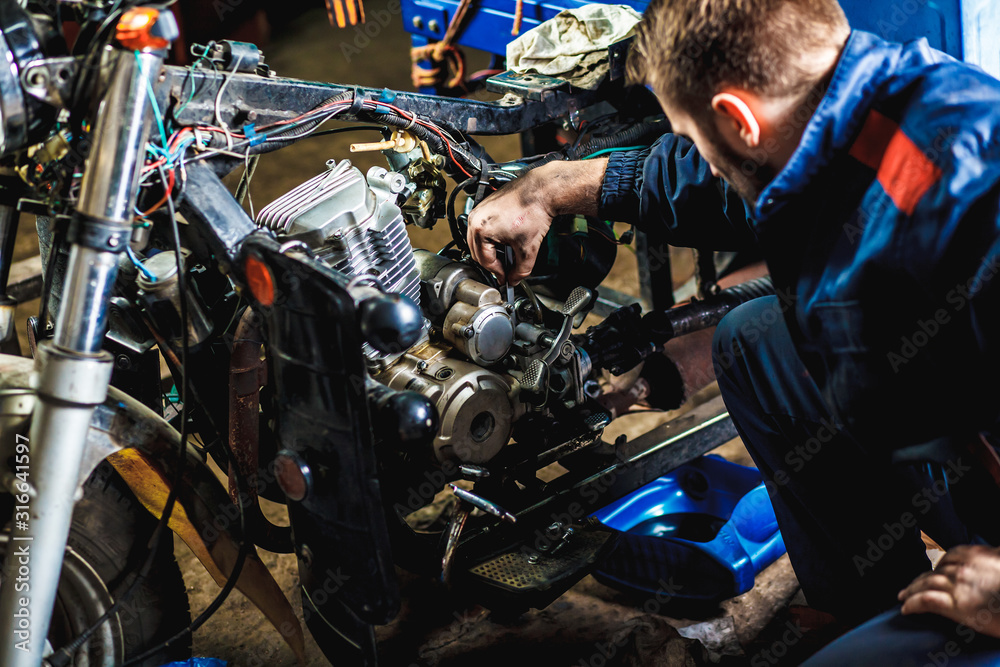 Specialist in coveralls working with motorized bicycles at repair garage. Motorcycle repair